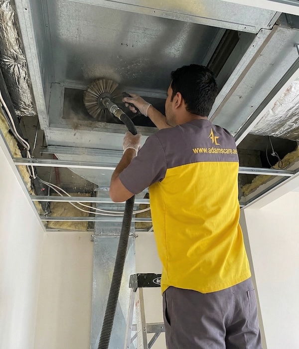 Adams Care Technician uses a rotary brush and vacuum on metal ductwork to provide professional AC cleaning Dubai quality