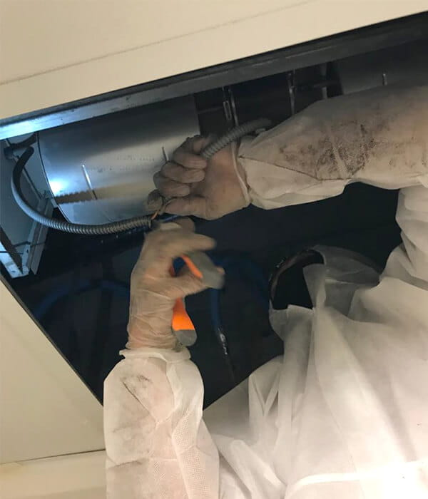 A worker in protective gear repairs an AC air duct, using tools with gloved hands. The setting is industrial, with a focus on maintenance and safety.