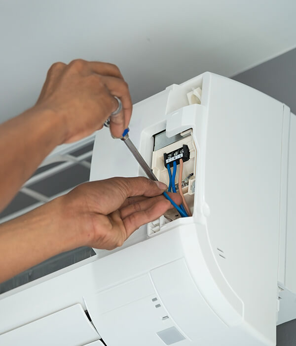 Hands repairing an air conditioner, using a screwdriver to adjust wiring. The focus is on the open unit, conveying a sense of careful maintenance.