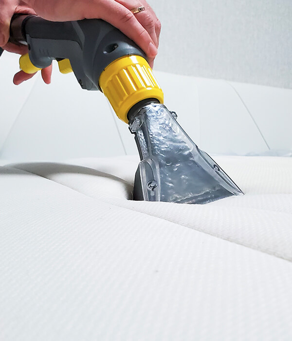 123 A close-up of a hand using a vacuum cleaner attachment to clean a white mattress.