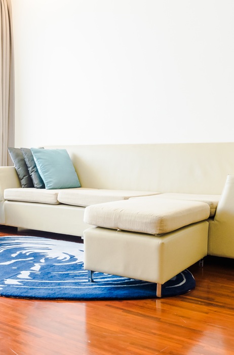 Modern living room with a beige couch, teal armchair, and round blue rug. White side table holds a small plant. Bright, minimalist atmosphere.