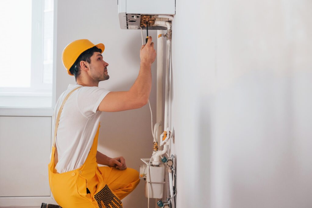 A technician in yellow uniform inspecting an AC, as part of the regular AC maintenance plans by Adams Care
