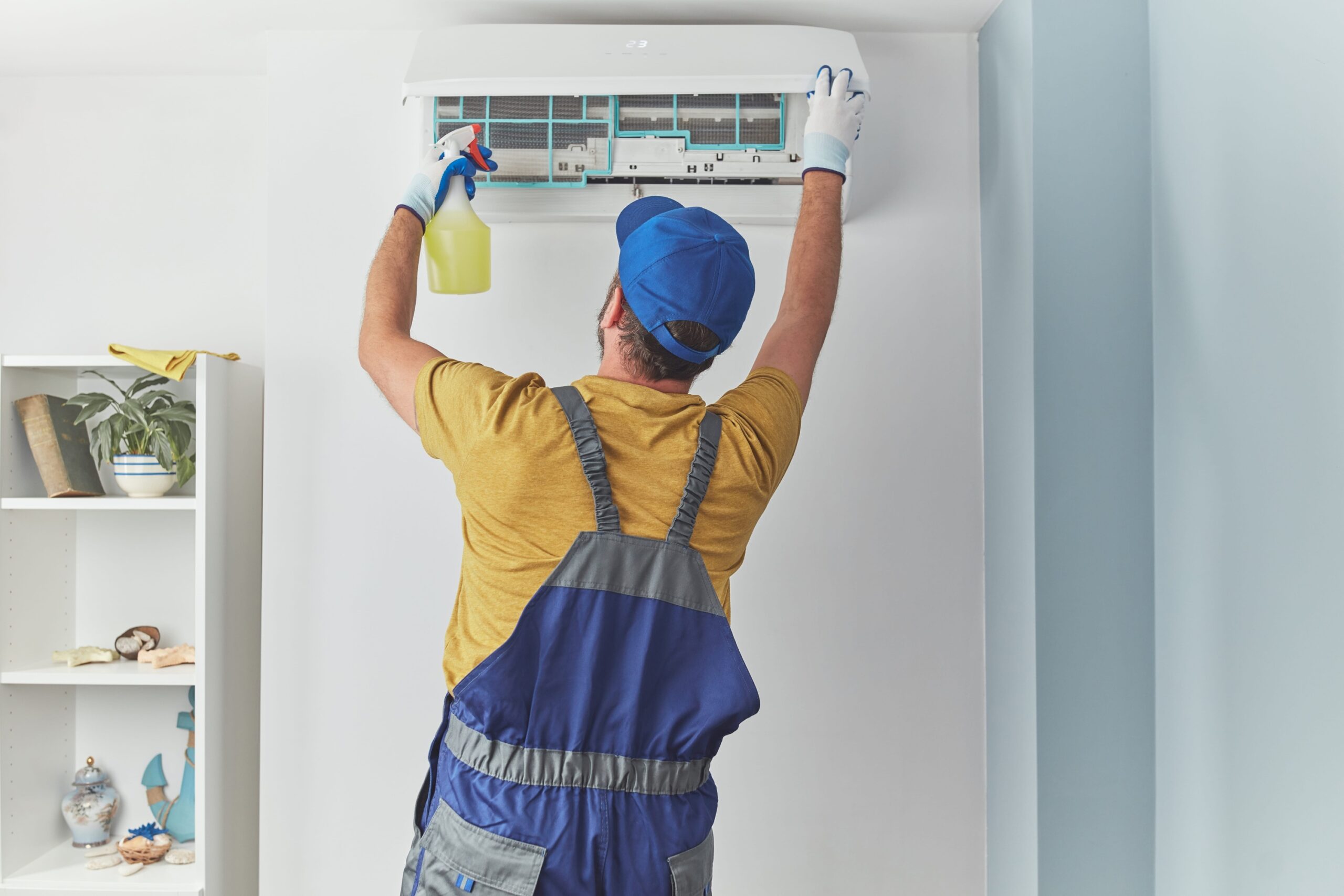 Repairman cleaning and fixing indoors AC unit, as part of ac maintenance plans, by Adams Care