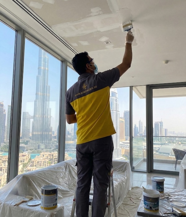 123 An Adams Care specialist brushes a white ceiling; high-reach waterproofing work overlooking the iconic Burj Khalifa.